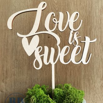 Zdjęcie przestawia drewniany cake topper dekoracyjny napis na tort Love is sweet i serduszko